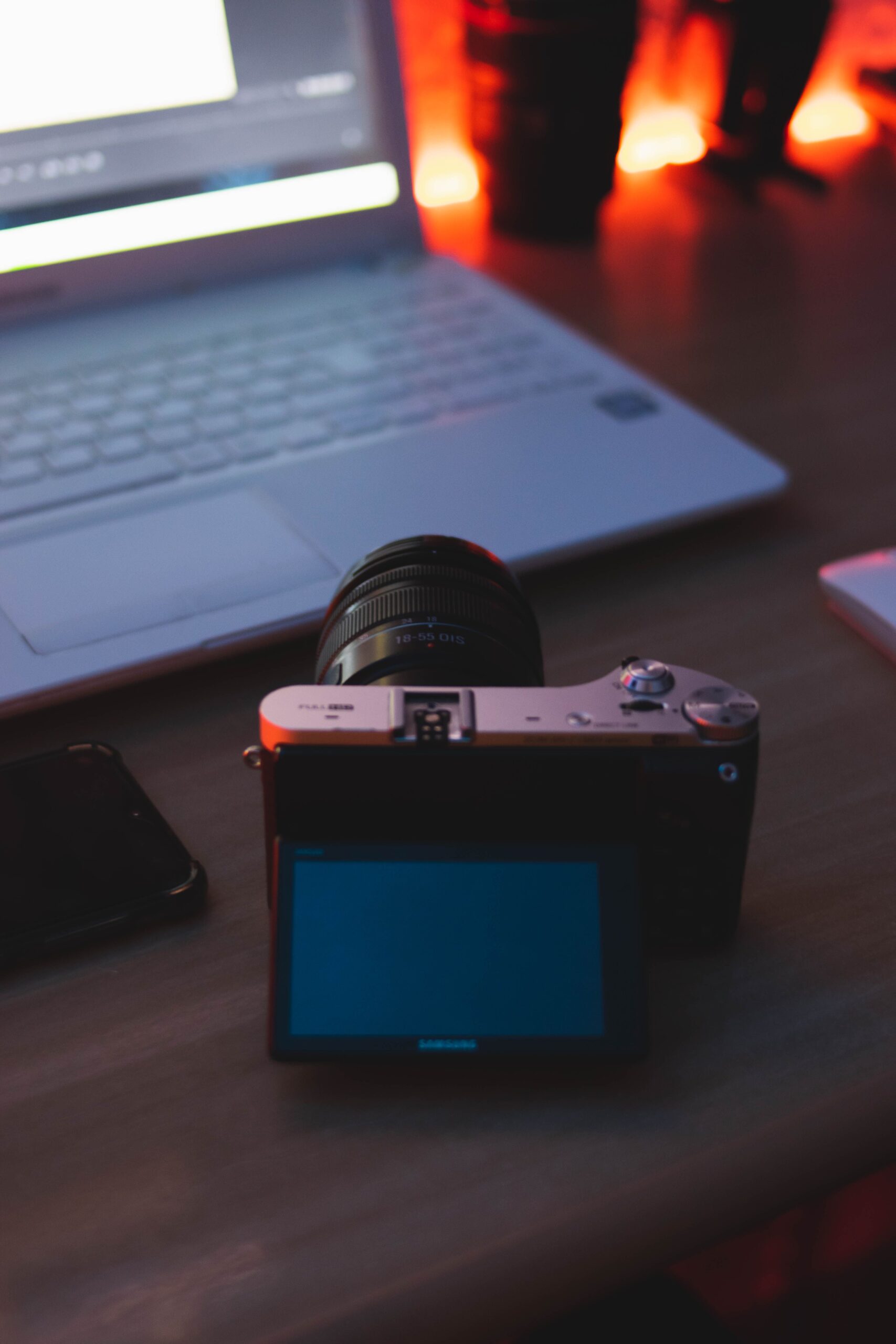 A camera with flip screen and laptop on a wooden desk with ambient lighting, perfect for creatives.